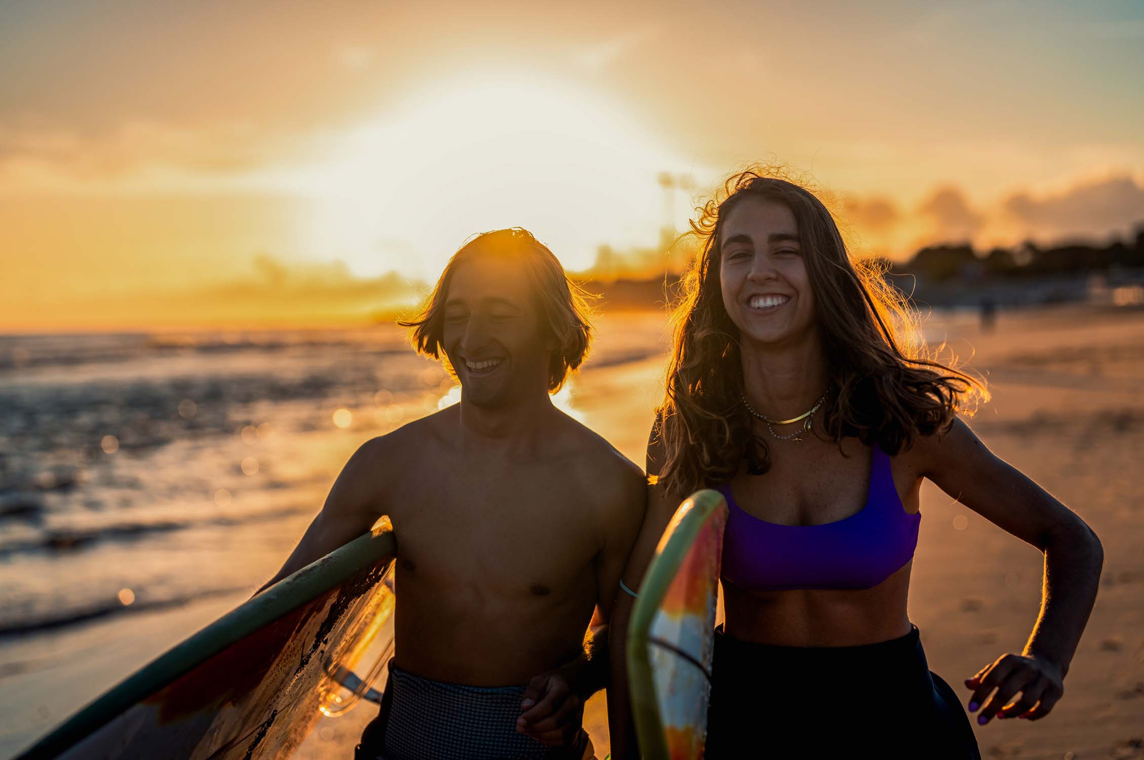 Two surfers with surfboard prepares to hit the waves at sunset.